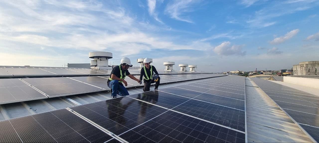 Two technicians in hard hats and safety vests checking a rooftop solar array